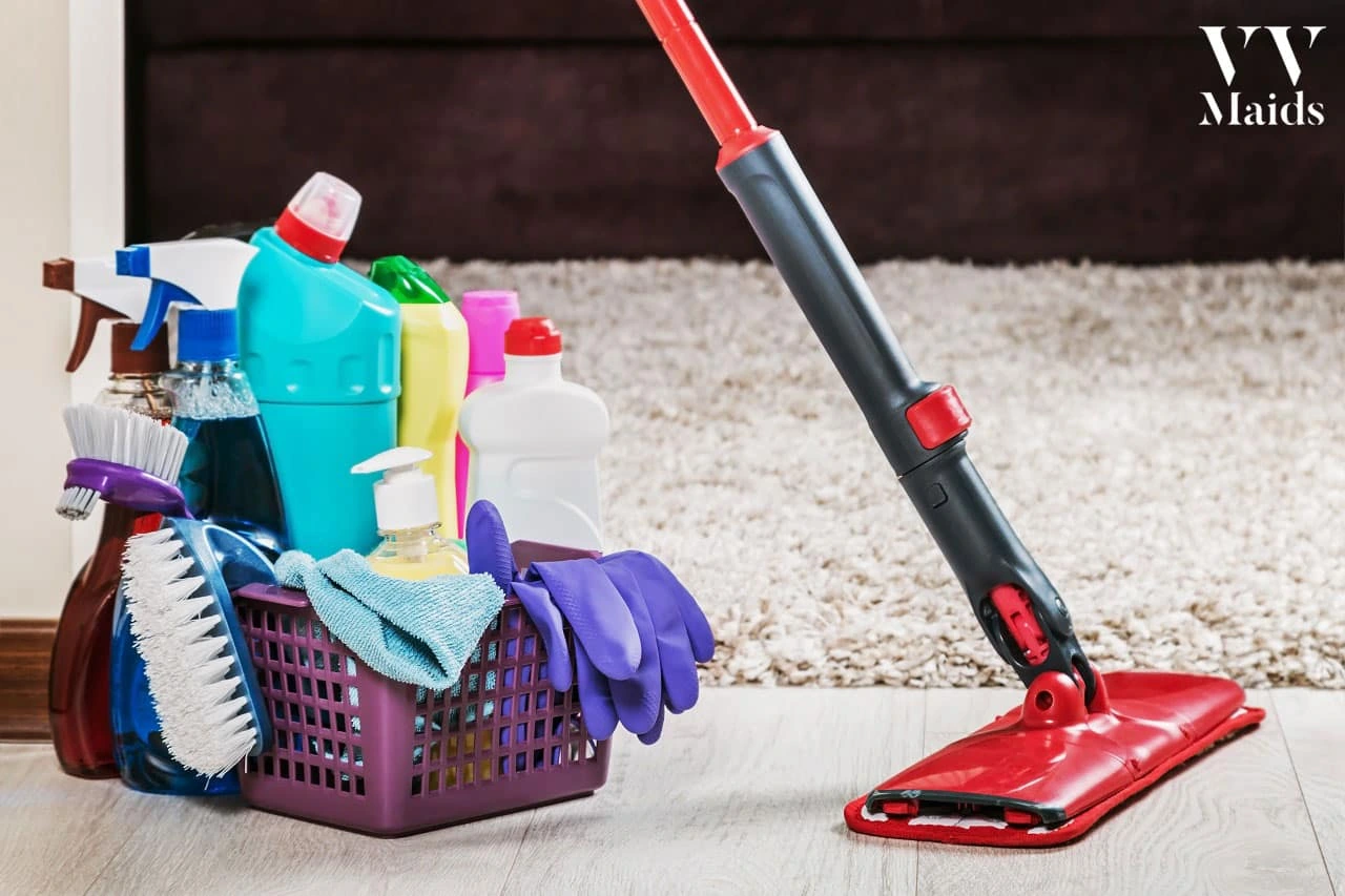 Different products for cleaning services A cleaning mop and various cleaning supplies are arranged neatly on a wooden floor, showcasing VV Maids Cleaning Services in NY.