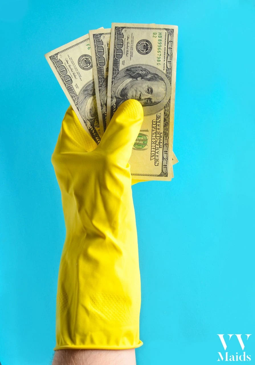 Cleaning Service Cost A hand in a yellow rubber glove holds three hundred-dollar bills against a blue background, representing VV Maids Cleaning