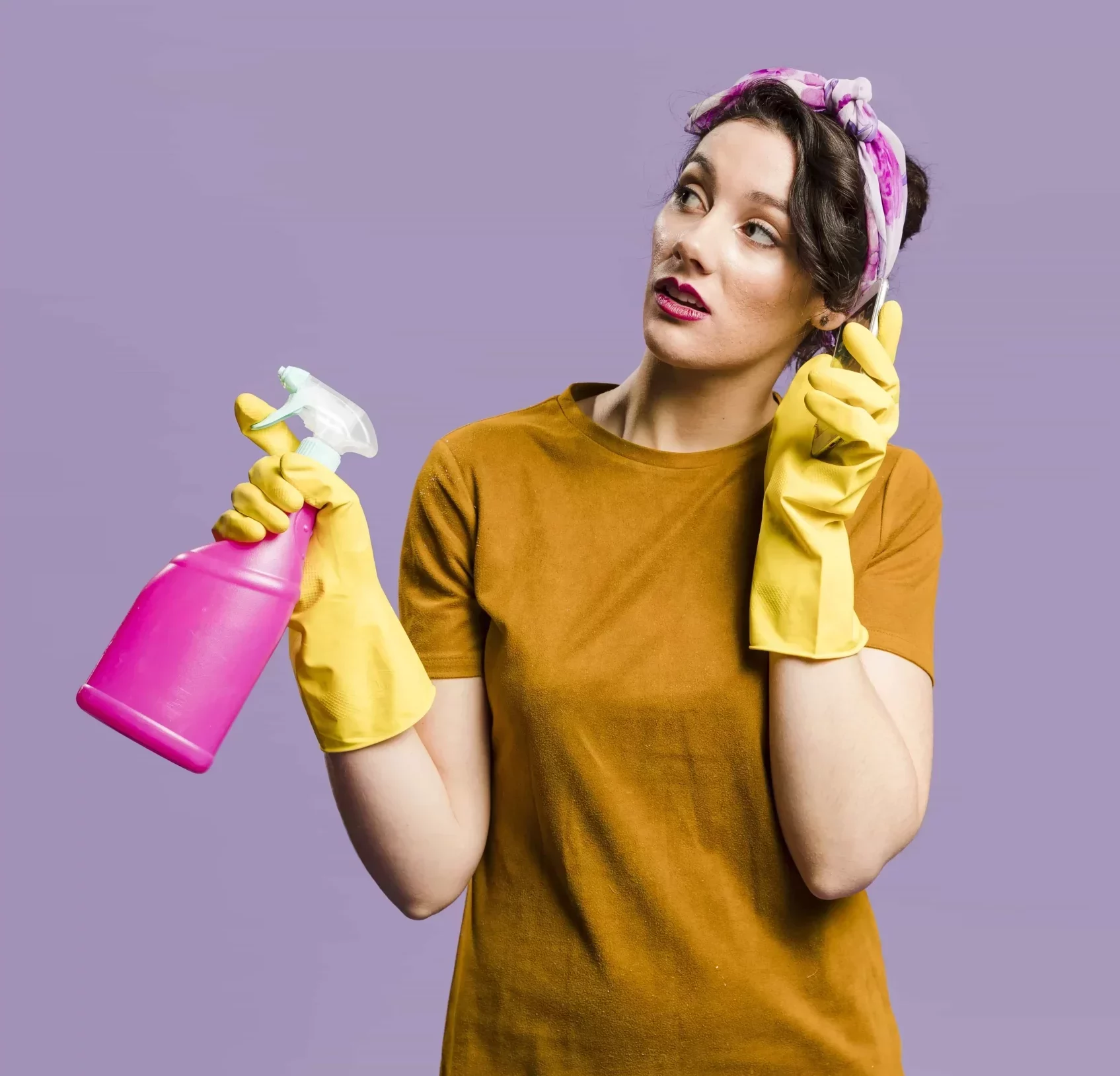 woman wearing a bandana and cleaning gloves holding a cleanser by one hand while talking with her phone