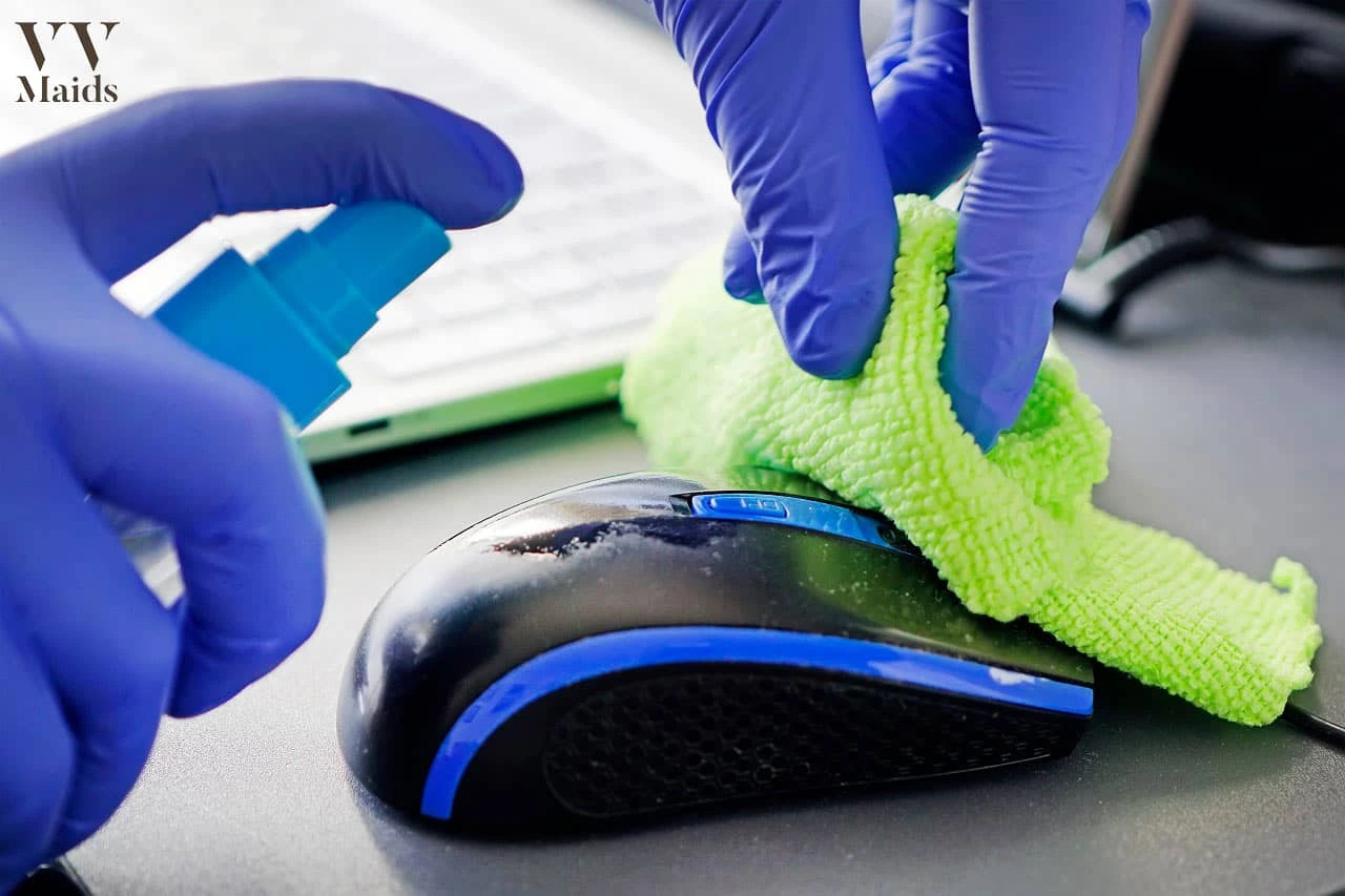 A gloved hand cleans a computer mouse with a green cloth, showcasing VV Maids Cleaning Services in NY.