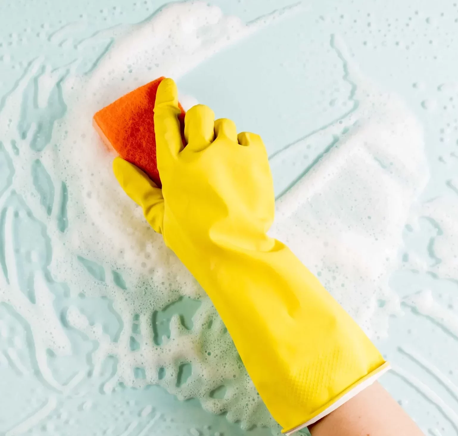 hand wearing yellow cleaning gloves holding a sponge to clean a surface with foam and suds