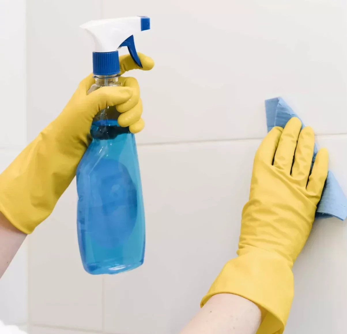 hands wearing yellow cleaning gloves using a cleanser and a wipe to clean a wall