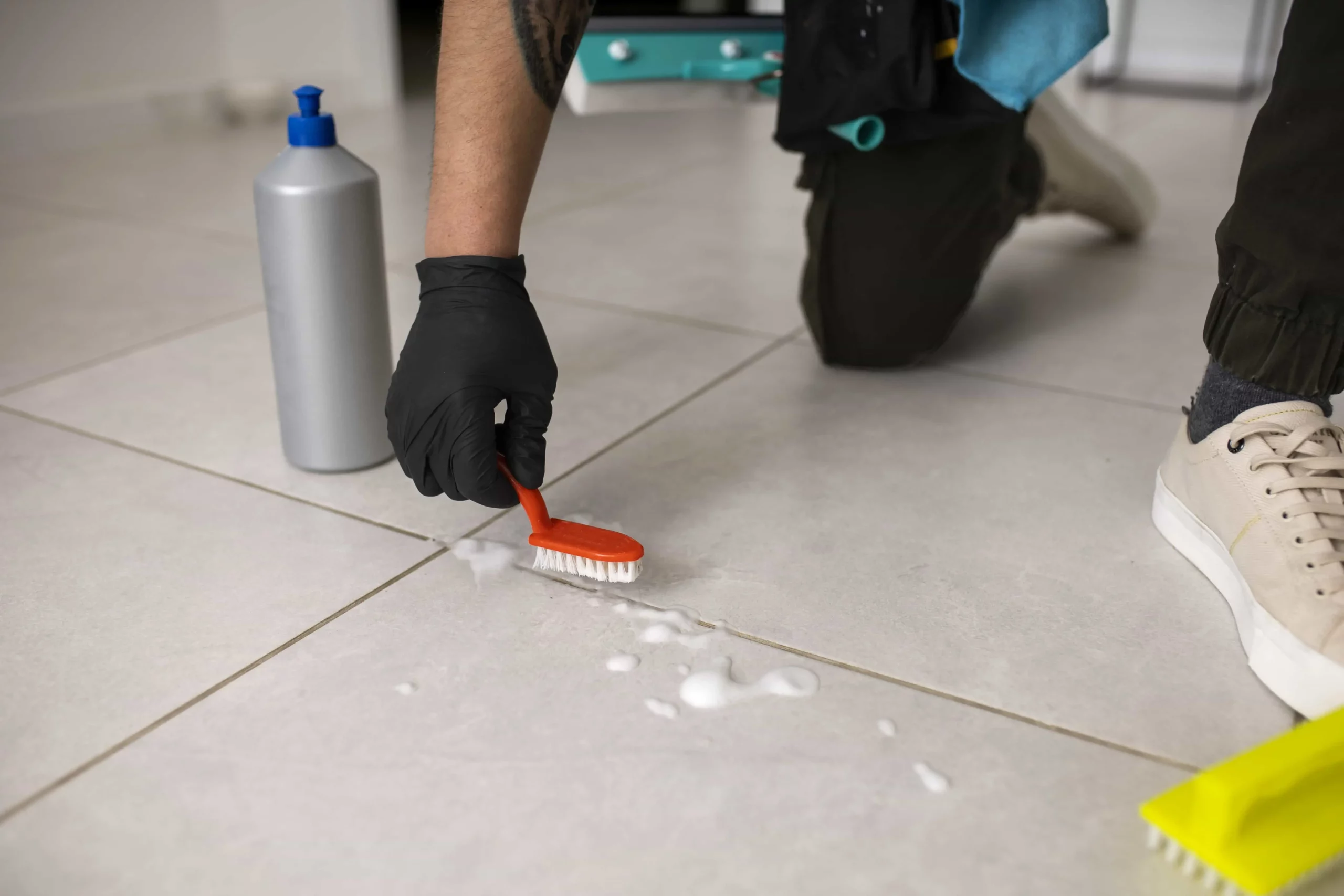 man cleaning grout on tile floor with a scrubber