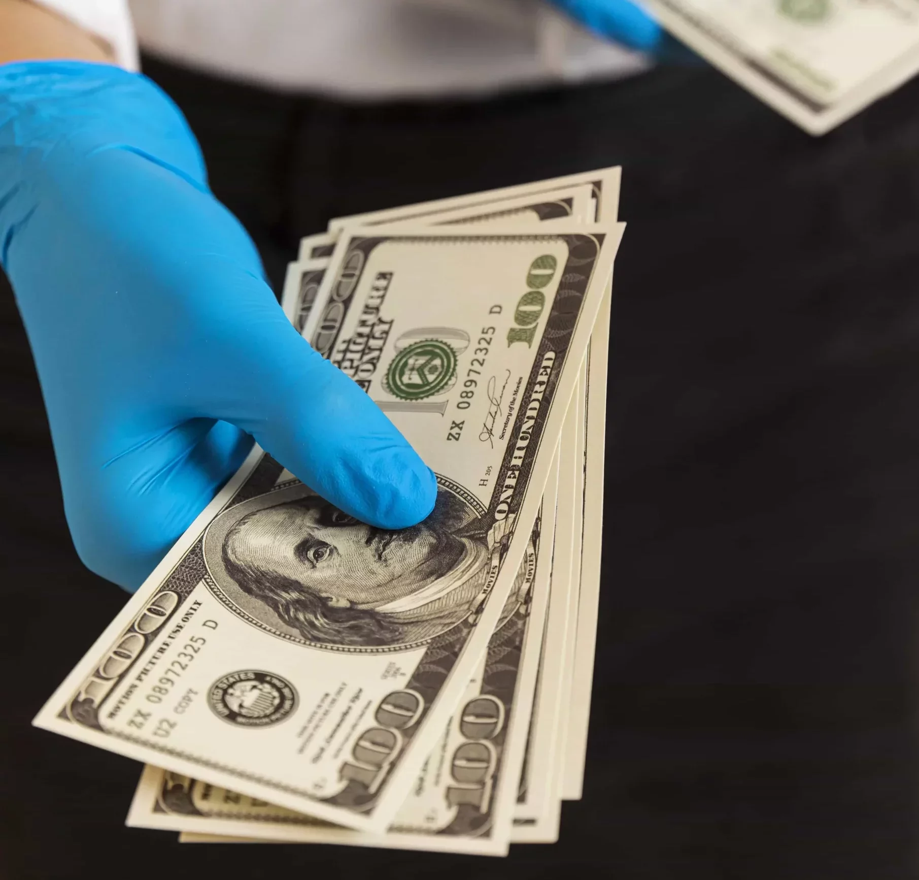 hand with blue gloves holding some dollar bills
