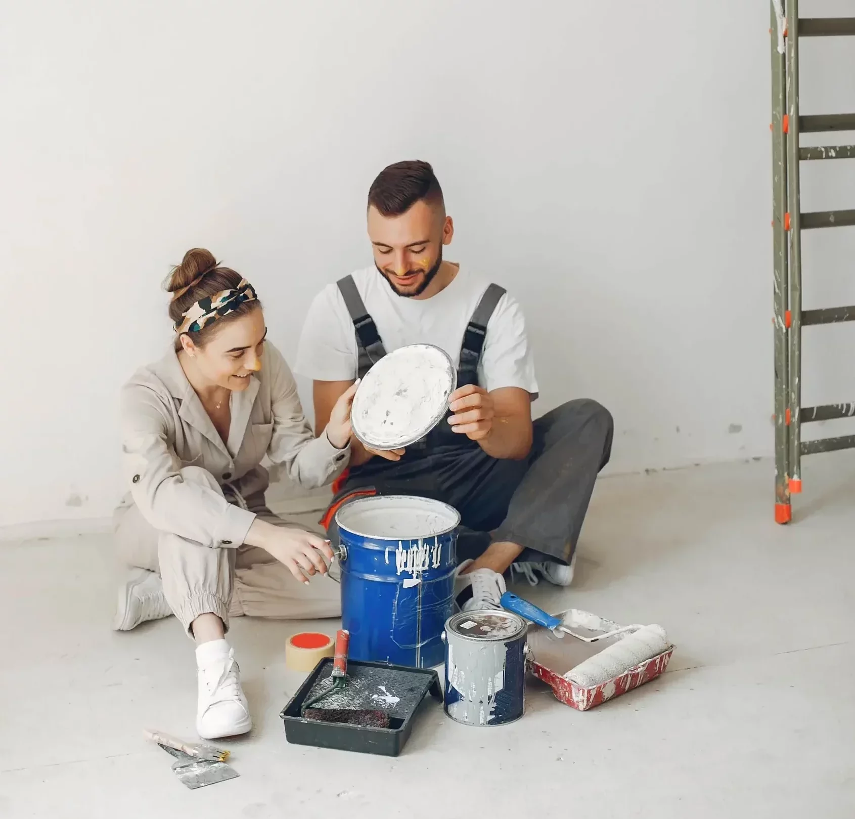 Young smiling couple sitting on the floor surrounded by painting equipment