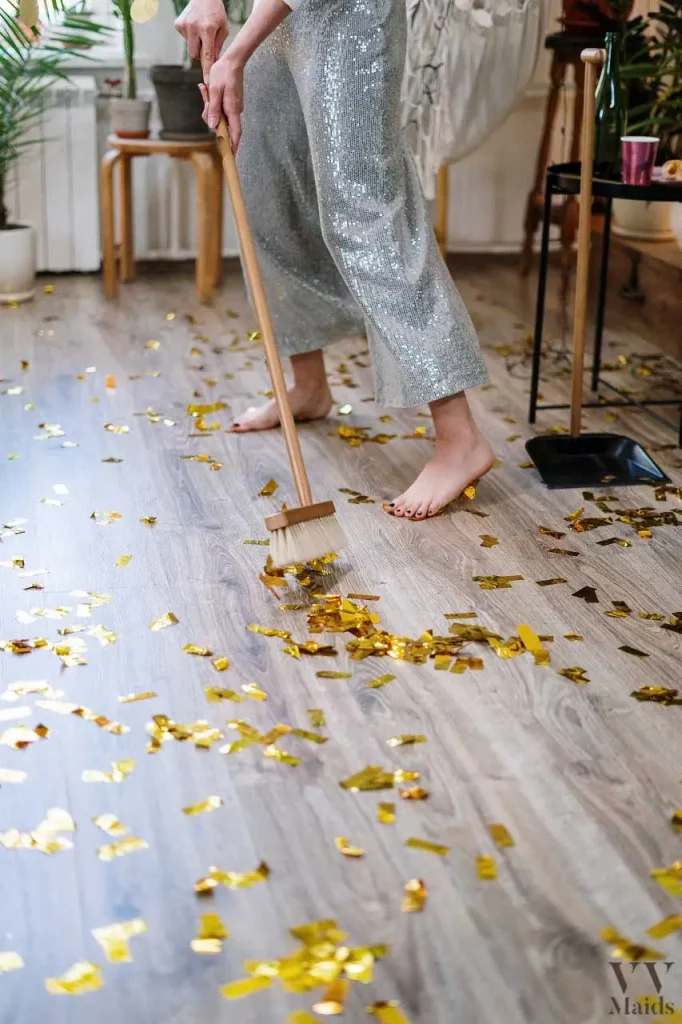 woman in sequin pants holding a broom and cleaning confetti off the floor after a party