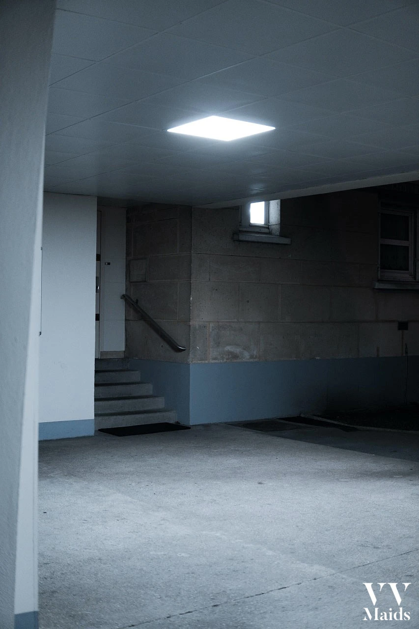 a dark basement with stairs and a small window on the wall with a single lamp on the ceiling