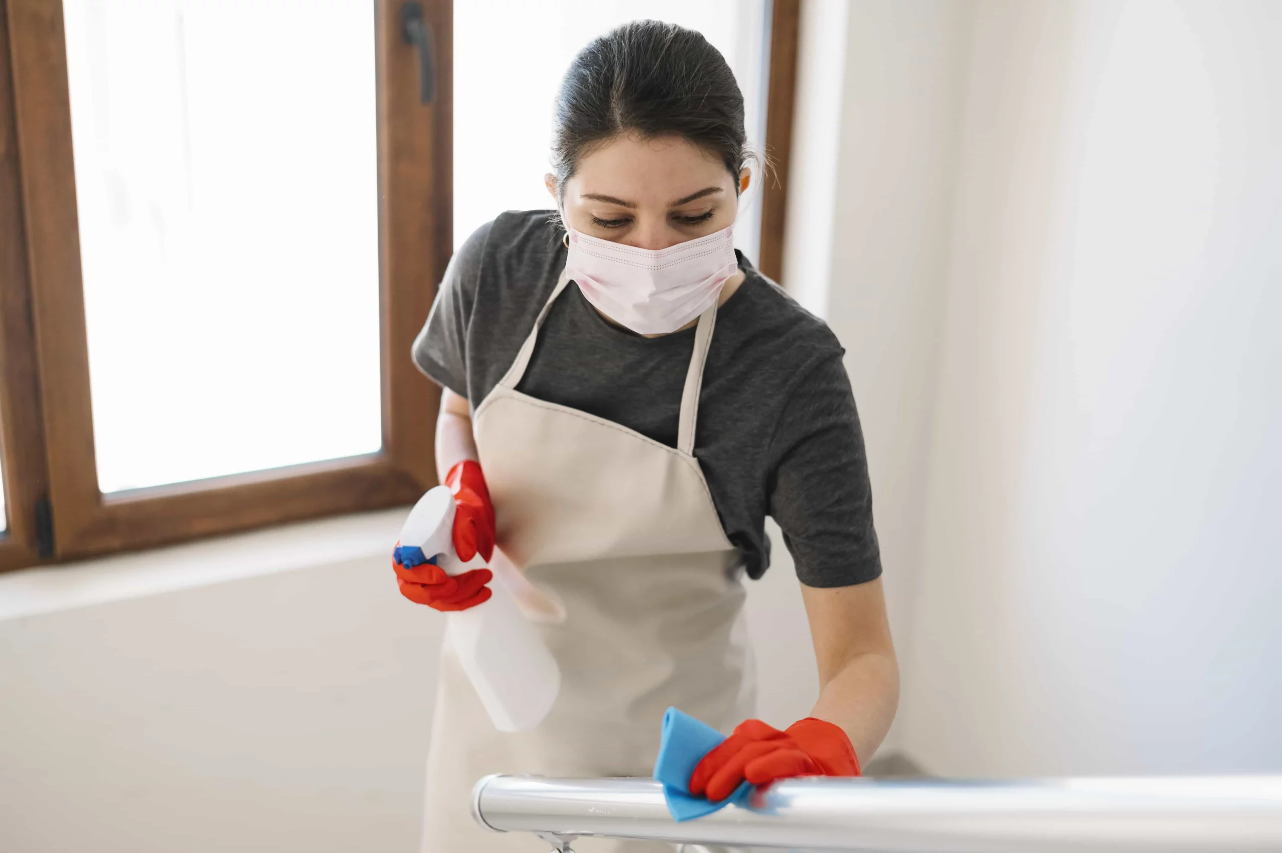 young cleaning lady wearing a mask and apron cleaning the staircases with a wipe