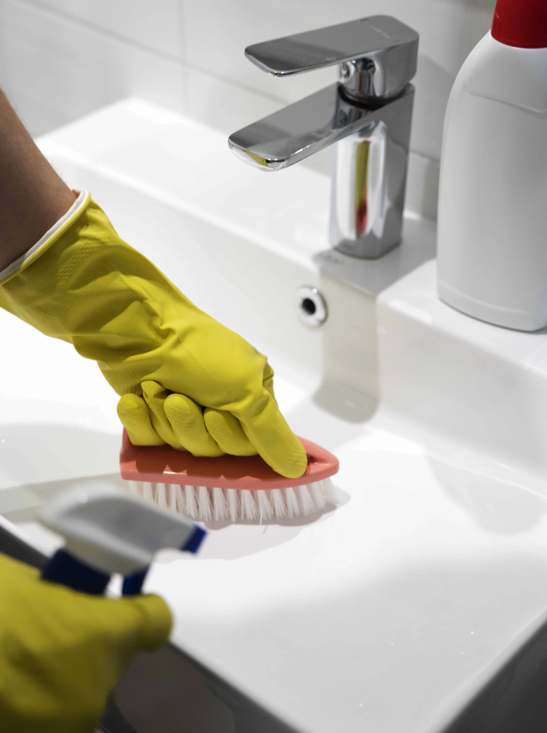 person's hands in cleaning gloves using a scrubber to clean the bathroom sink