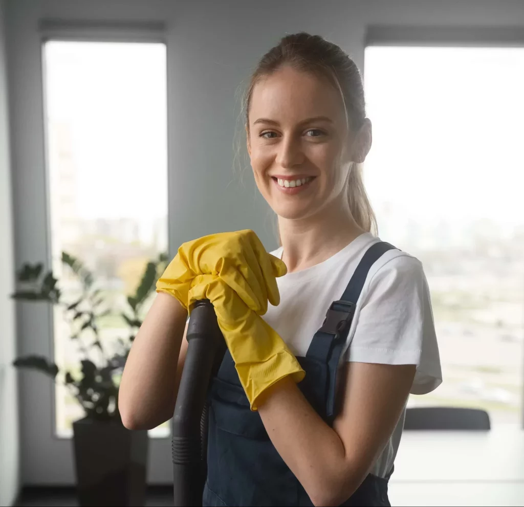 smiling female professional cleaner holding onto a mop with cleaning gloves