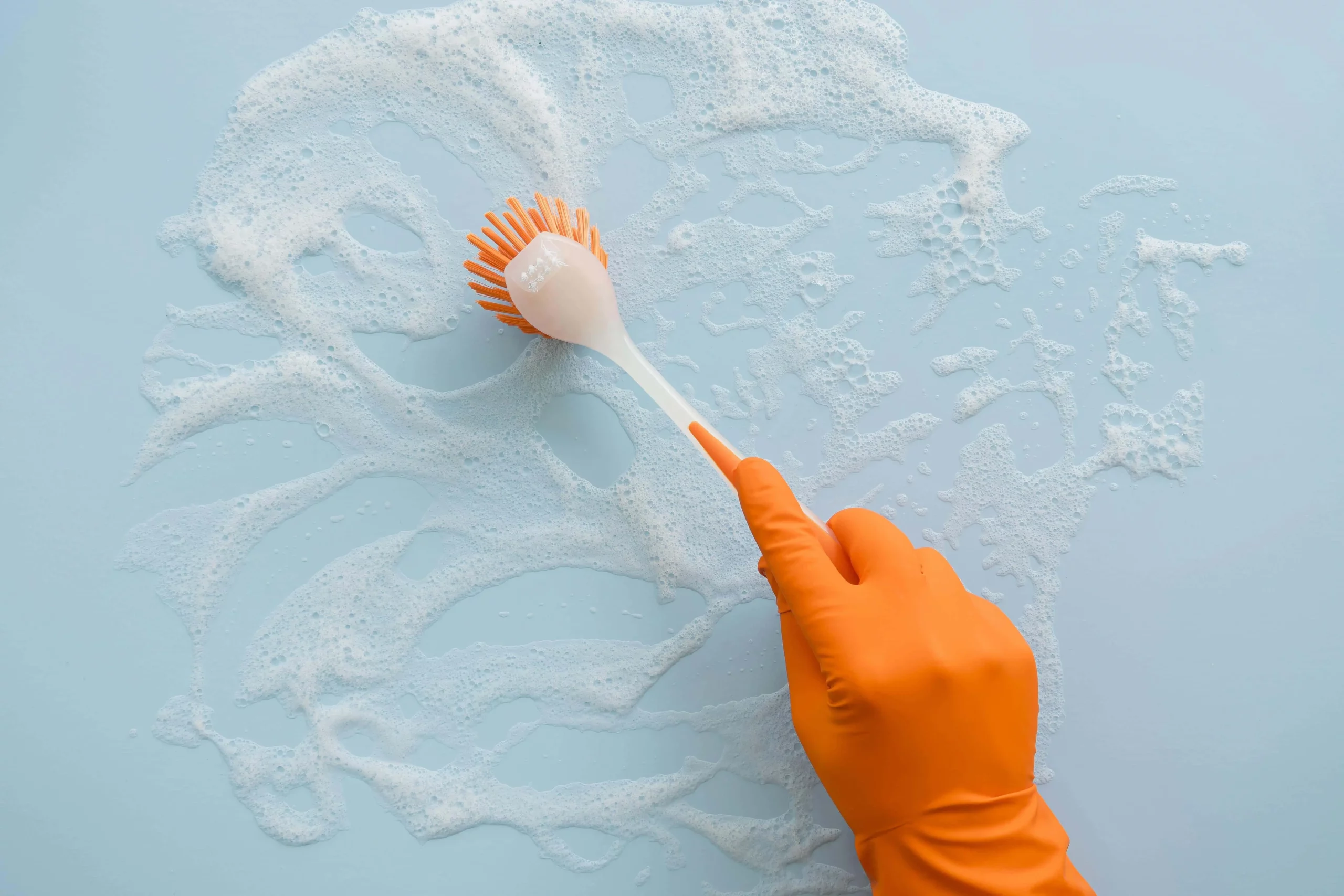 hand with orange glove scrubbing a surface with a brush to clean stains
